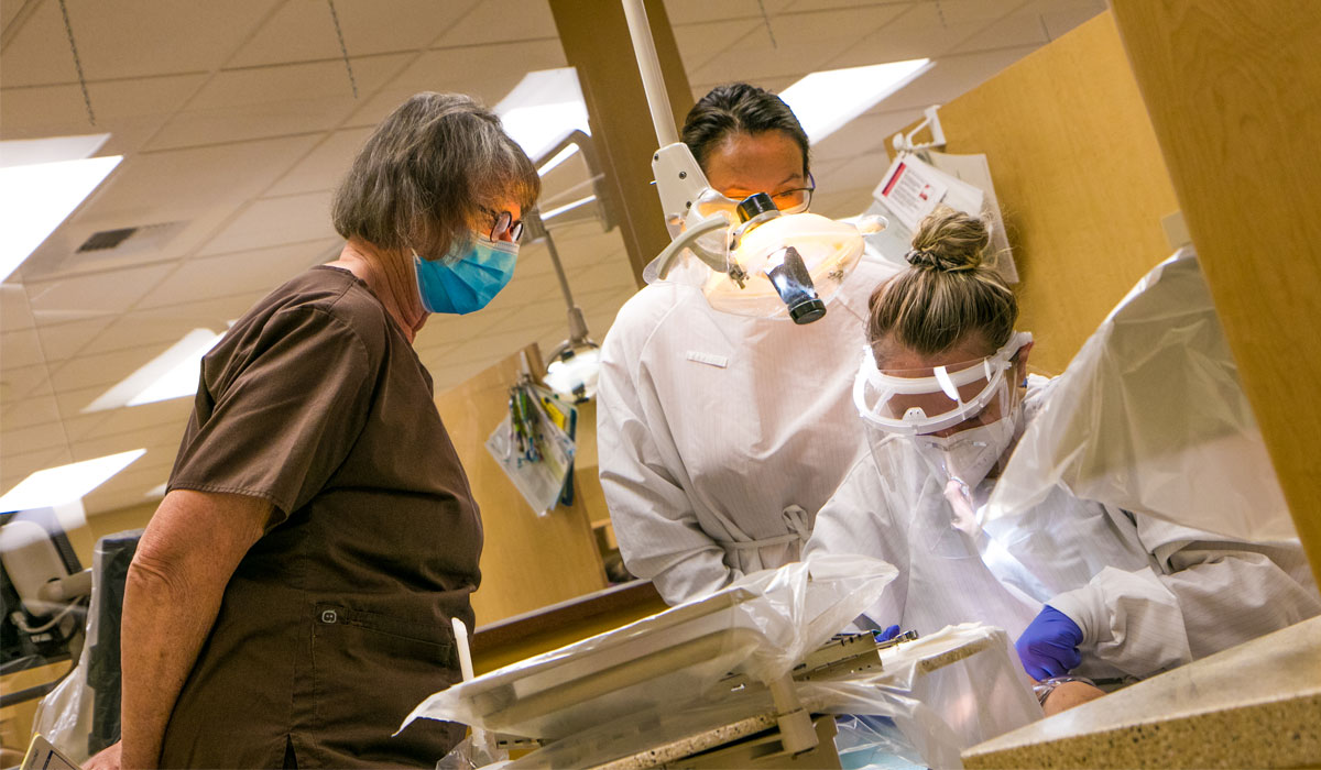 Two students work on a mock dental procedure with instructor.