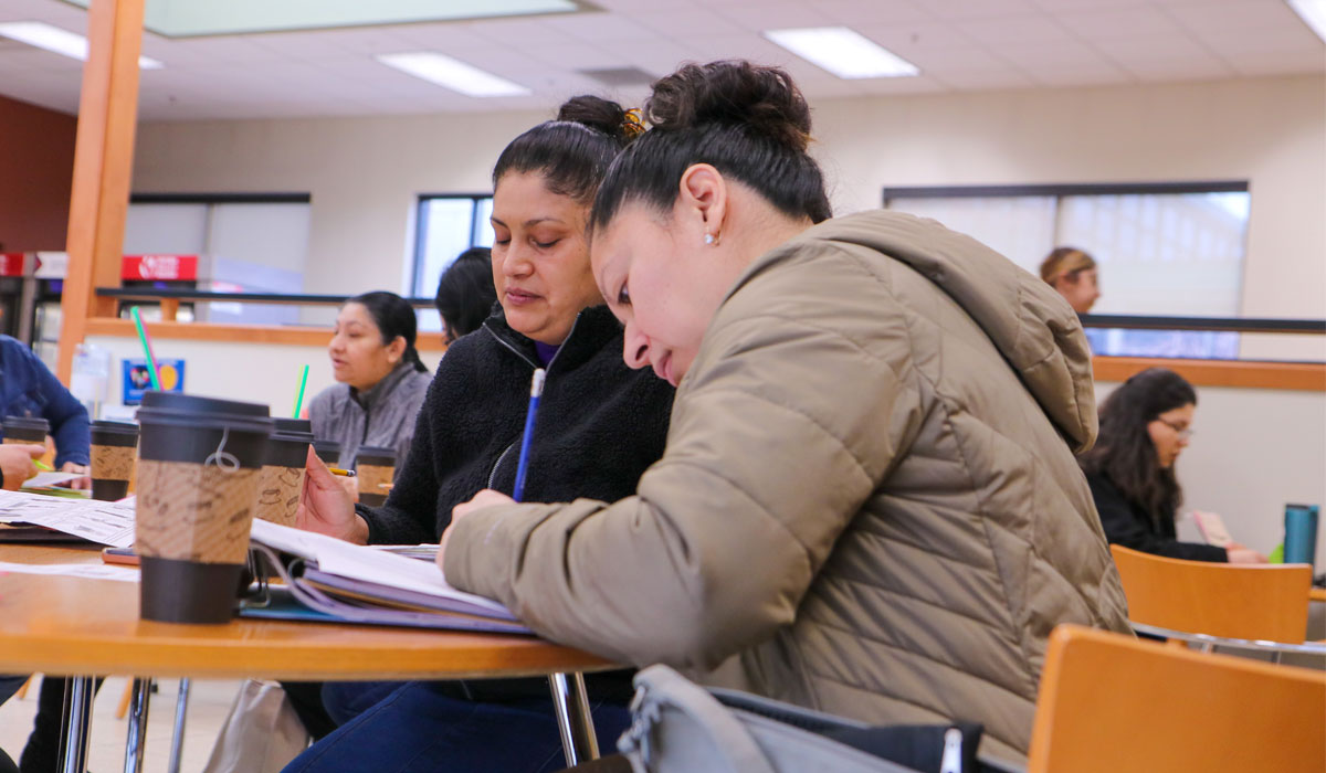 Student sitting in campus common area writing in her notebook. 