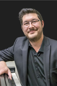 Jeff Kaschmitter poses for picture sitting at a piano. 