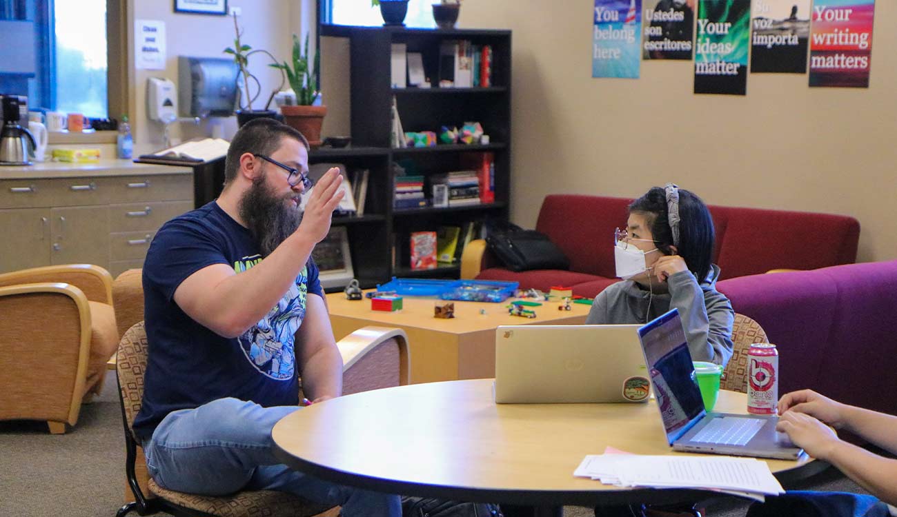 Writing tutor talks with student at table