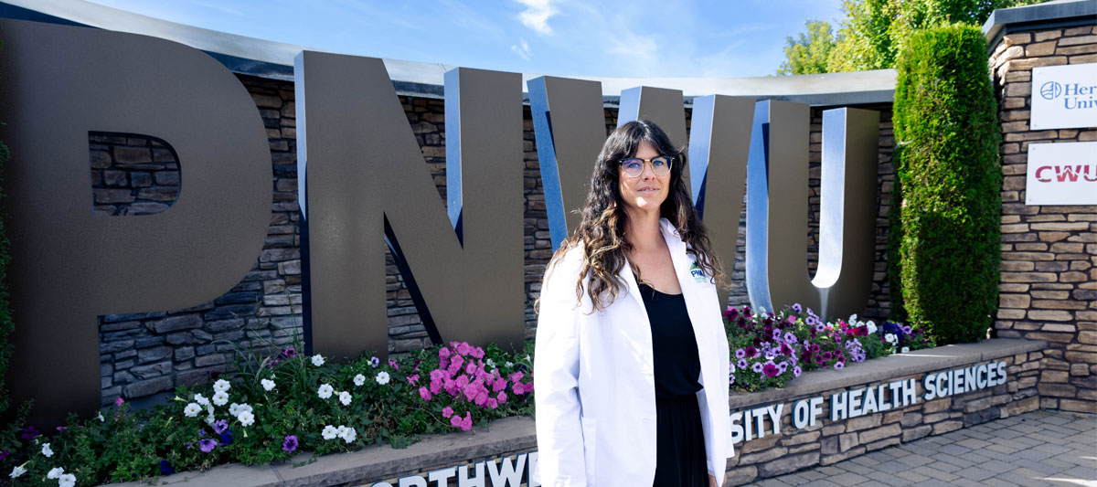 Former YVC student poses for picture infront of PNWU sign. 