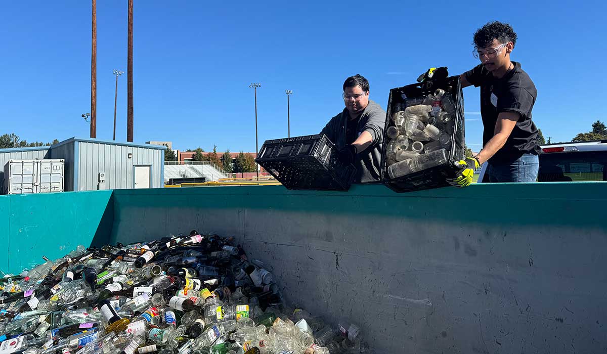 STEM students dump glass bottles into a bin for recycling