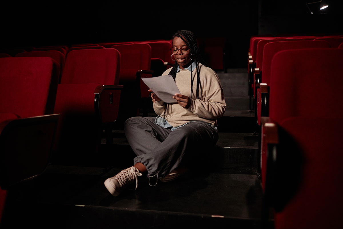 Female sitting on theatre floor reading a paper