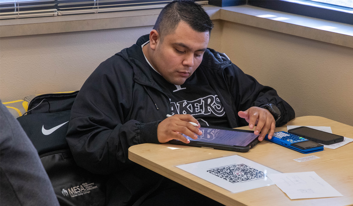 Student sitting at table working on math assignment with calculator. 