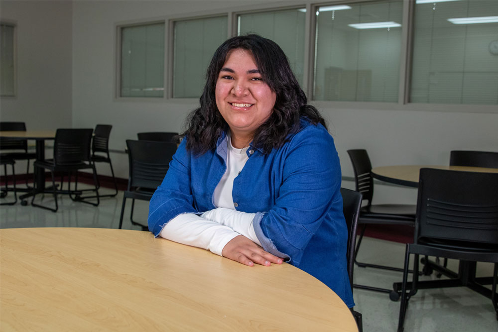 Jeanette Martinez poses for student story picture sitting at table in a YVC classroom. 