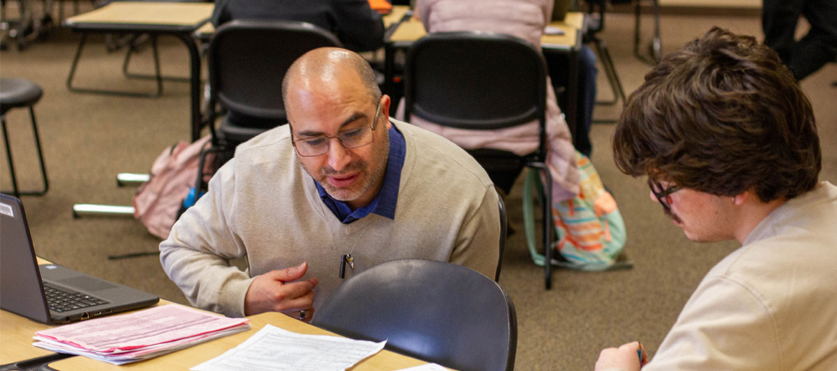 YVC staff member leans over a table to assist a student during advising day. 