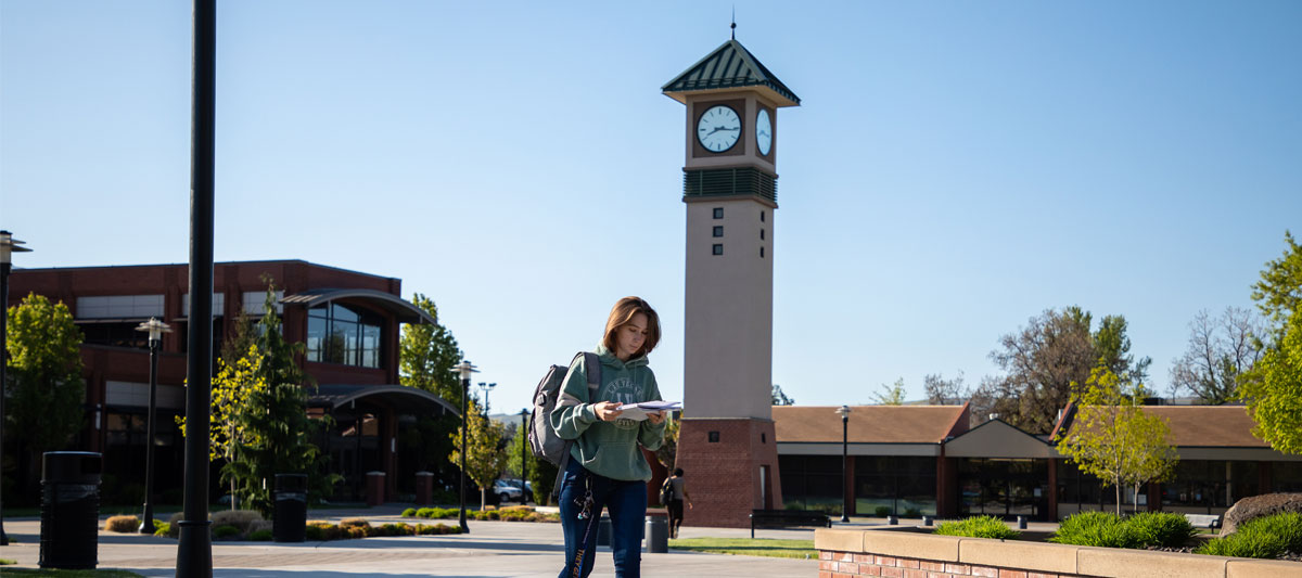 Student walking through Yakima Campus with clock tower in the background.