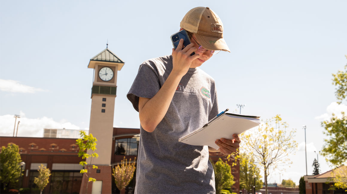 Student on his phone with YVC Clock Towere in the background. 