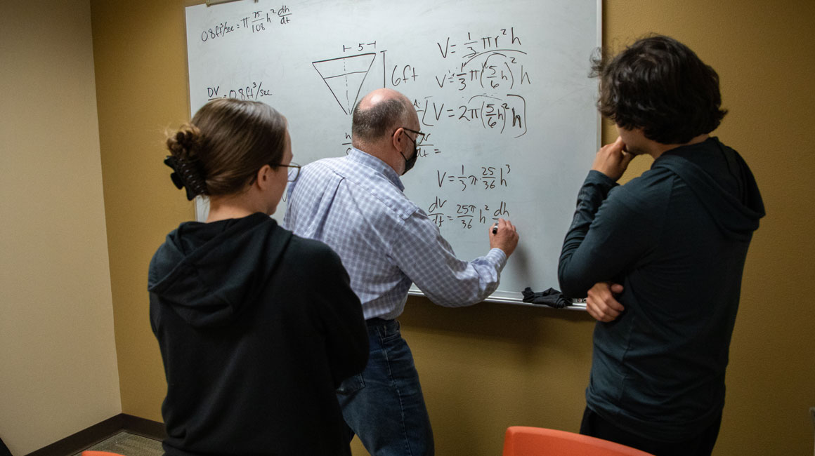 YVC math professor writes out problem on the board while two students look on. 