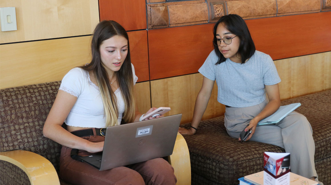 Two students works on a computer in a YVC cooridor.