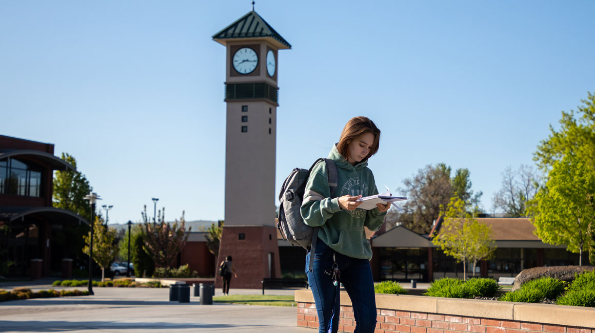 Student walks across the Yakima Campus with the Clock Tower in the background.