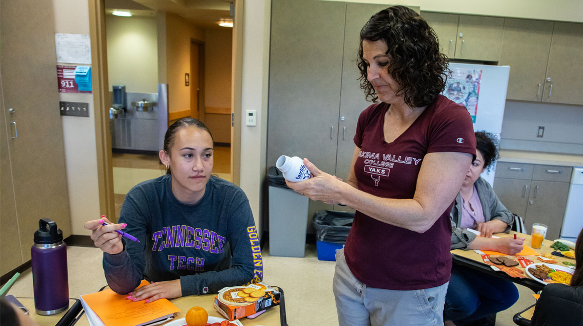 Instructor assists a student at their desk during class. 